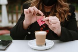 Young woman opening artificial sweetener packet to add to coffee